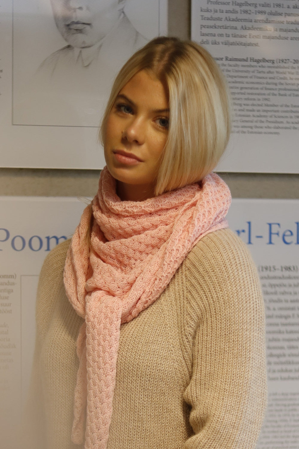 Woman wearing a pink scarf standing in front of a wall with biographical posters.